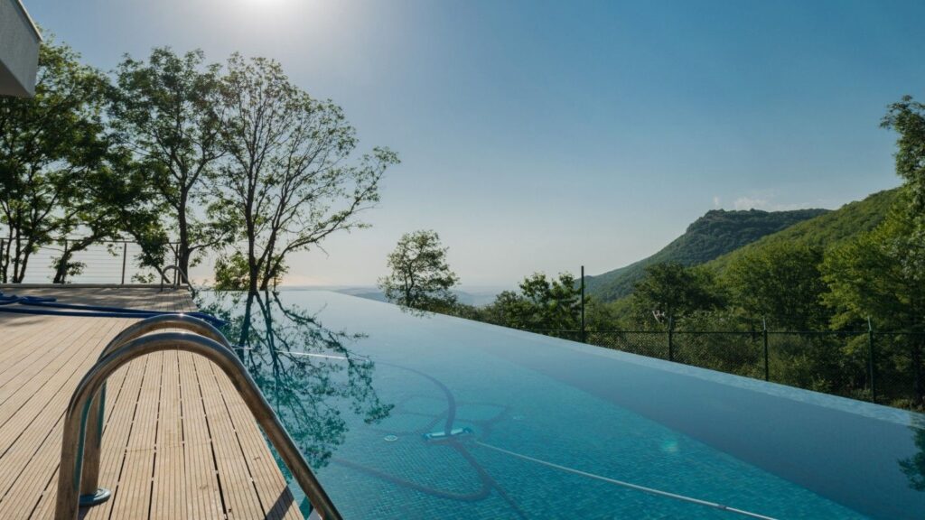 An infinity pool in the backyard of a home surrounded by green hills.