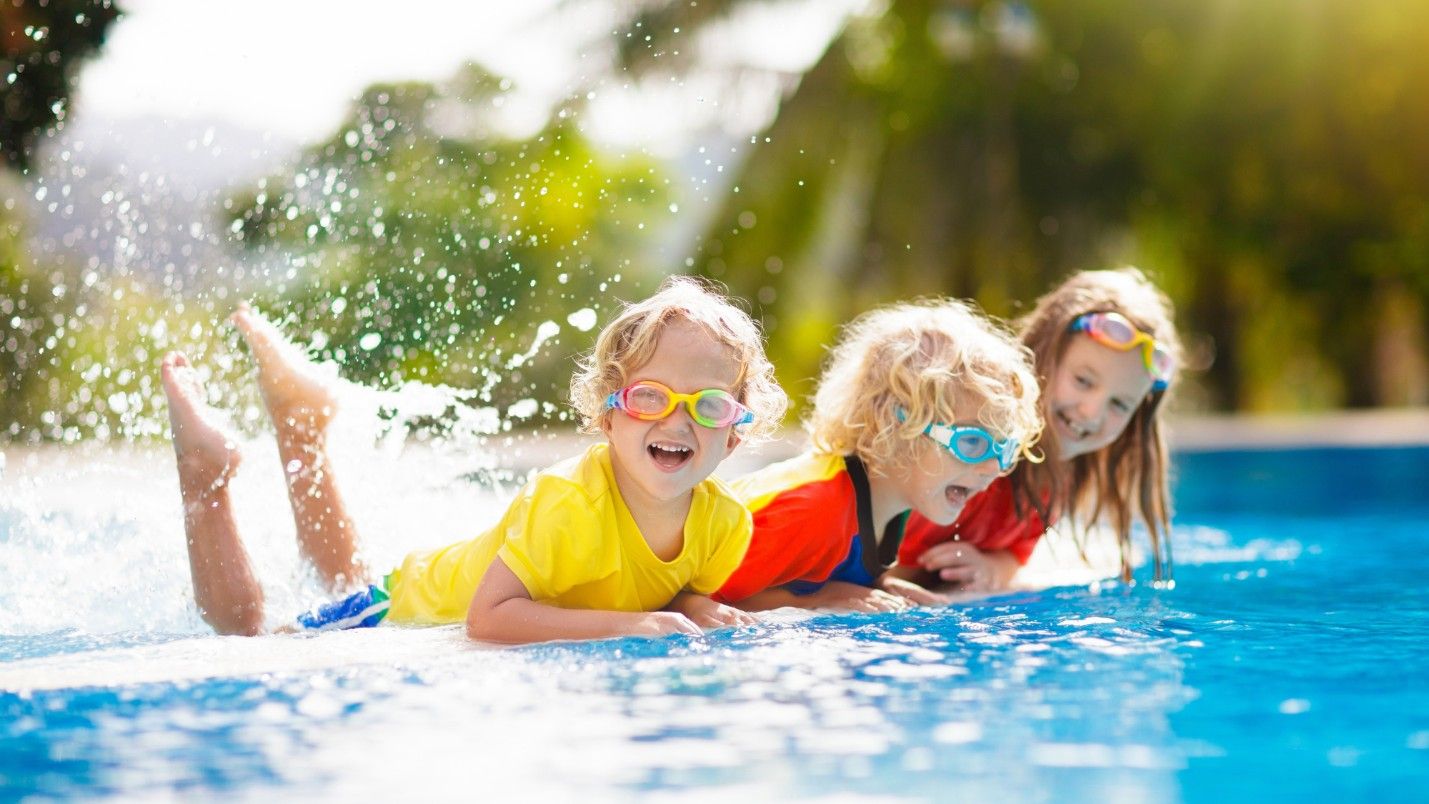 Three kids with swim goggles are playing in a pool.