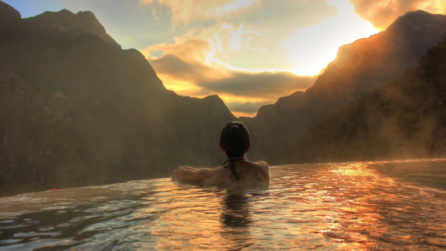 A woman in a mountain resort rests on the edge of an infinity pool.
