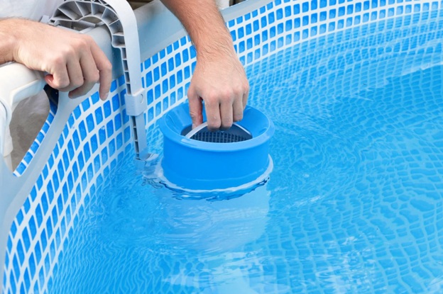 A person reaching their hand into a pool to clean up the filter basket.
