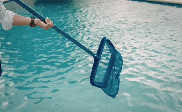A person wearing a watch, holding a long blue skimmer above a cleaned pool.